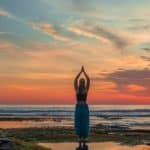 Silhouette of woman on beach with hands raised and in namaste mudra pointing to sky symbolising holding a spiritual vision to end conflict in life